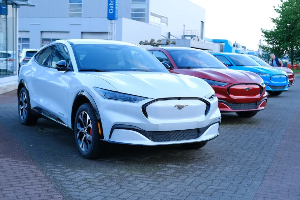 Row of white, red, and blue electric Ford Mustang Mach-E cars at dealership in Frankfurt, Germany.